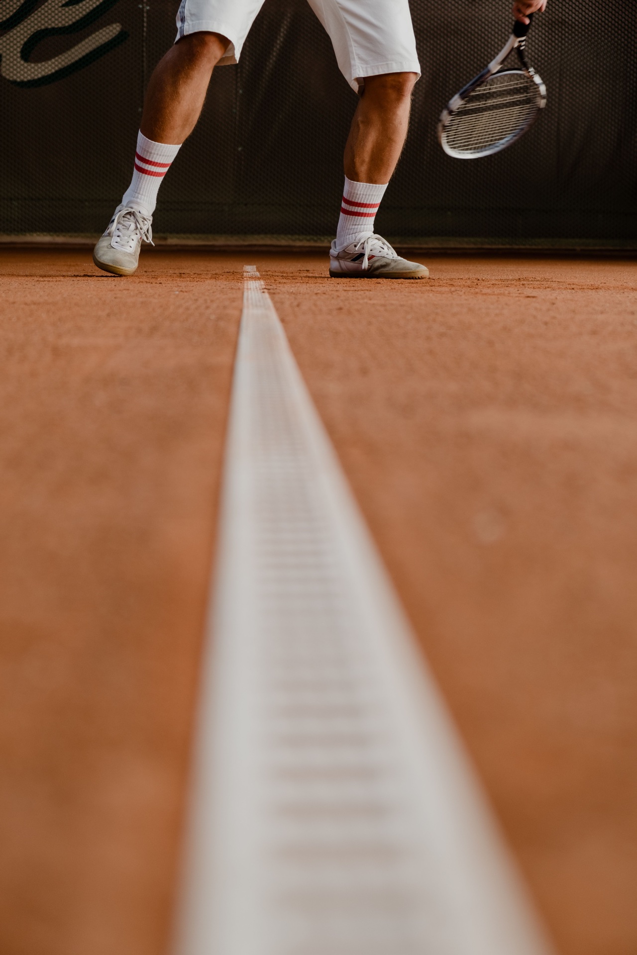 Tennis shoes and a racket at the baseline of a clay court.