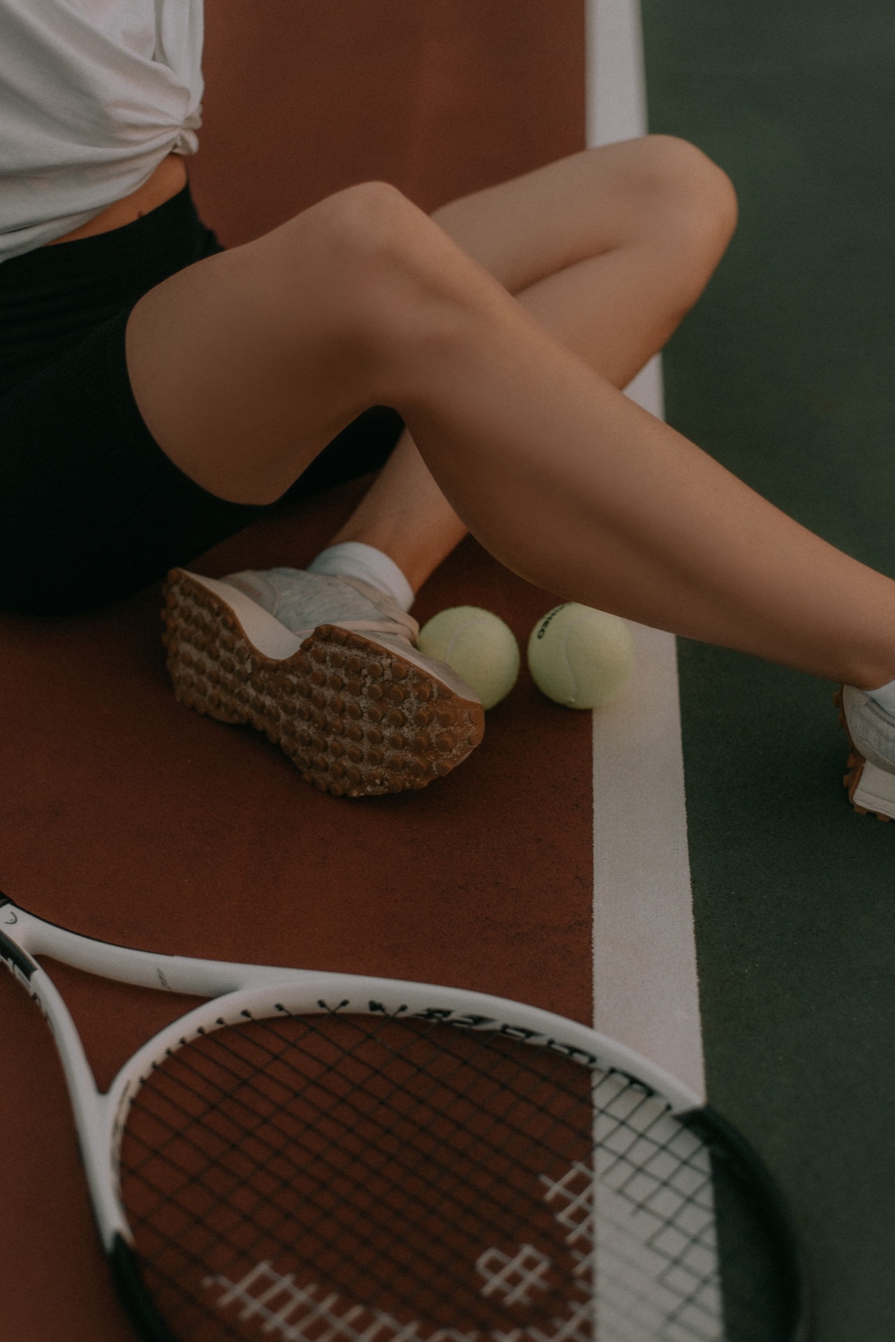 A racket, tennis shoes and balls beside a court line.