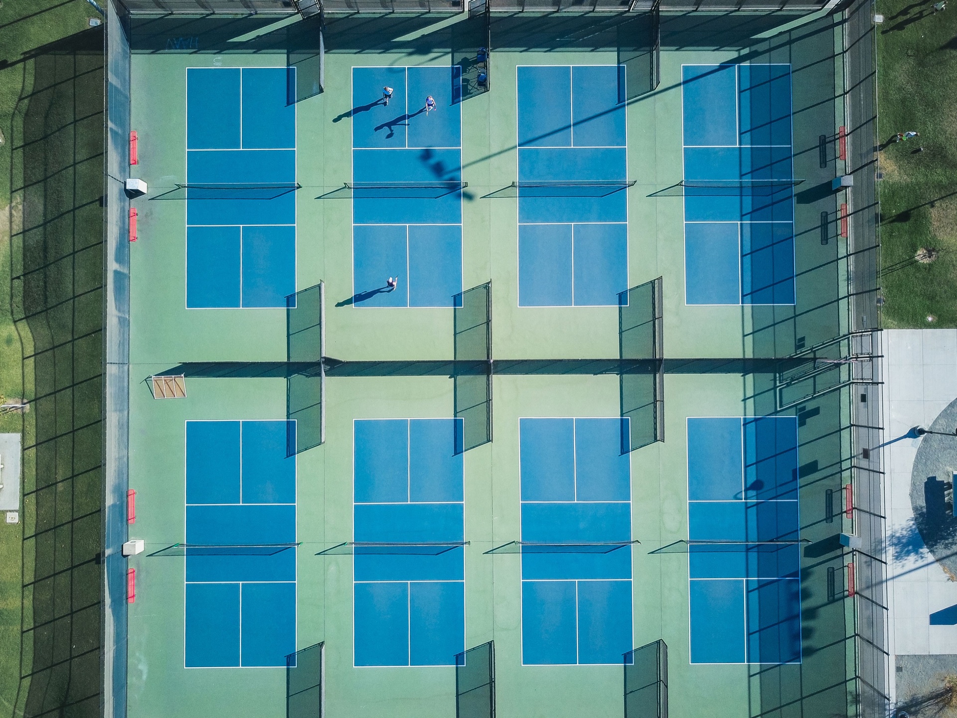 An aerial view of blue tennis courts crossed by long shadows.
