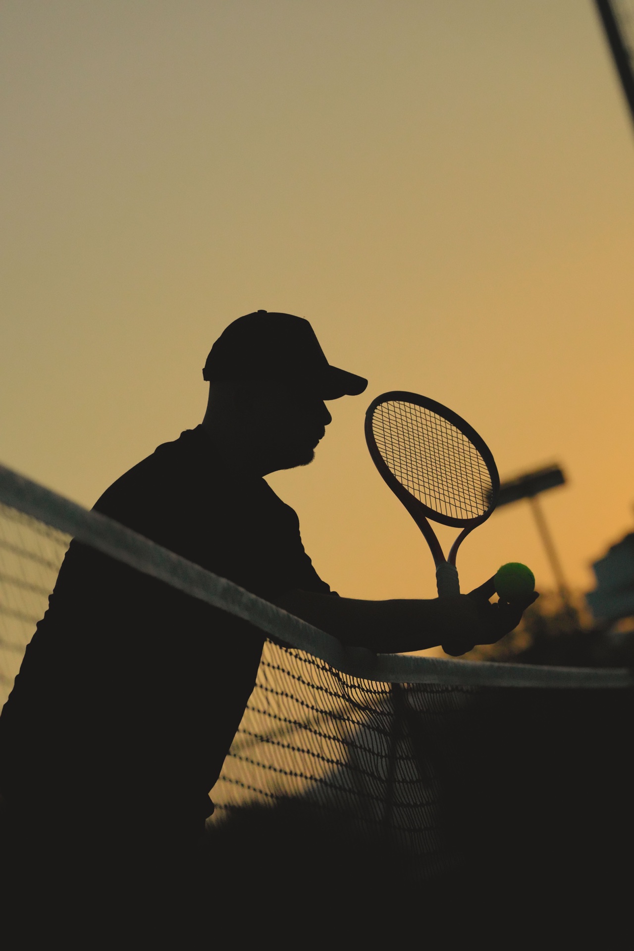 A tennis player holding a racket and ball in silhouette at sunset.